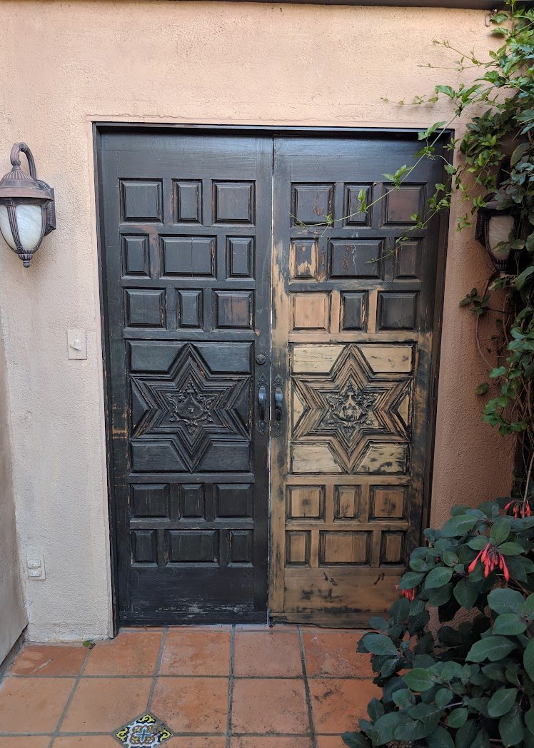 Carved double door with old black coating peeling away, one leaf stripped to bare wood