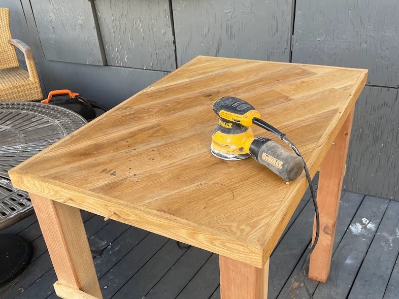 Small square table being sanded on the deck